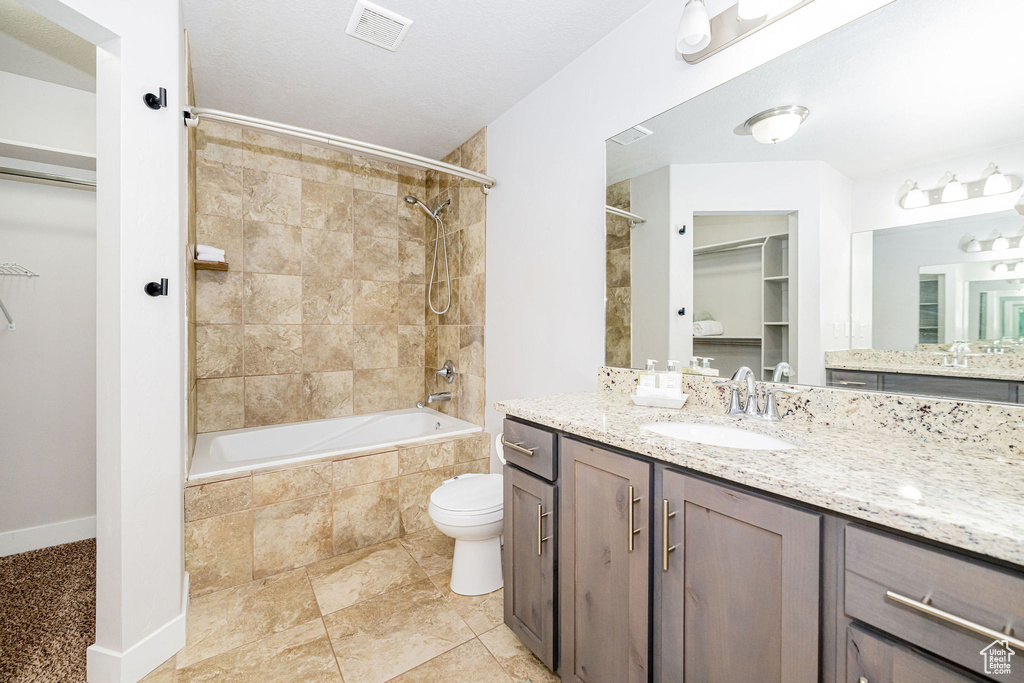 Full bath featuring a spacious closet, tiled shower / bath, vanity, toilet, and baseboards
