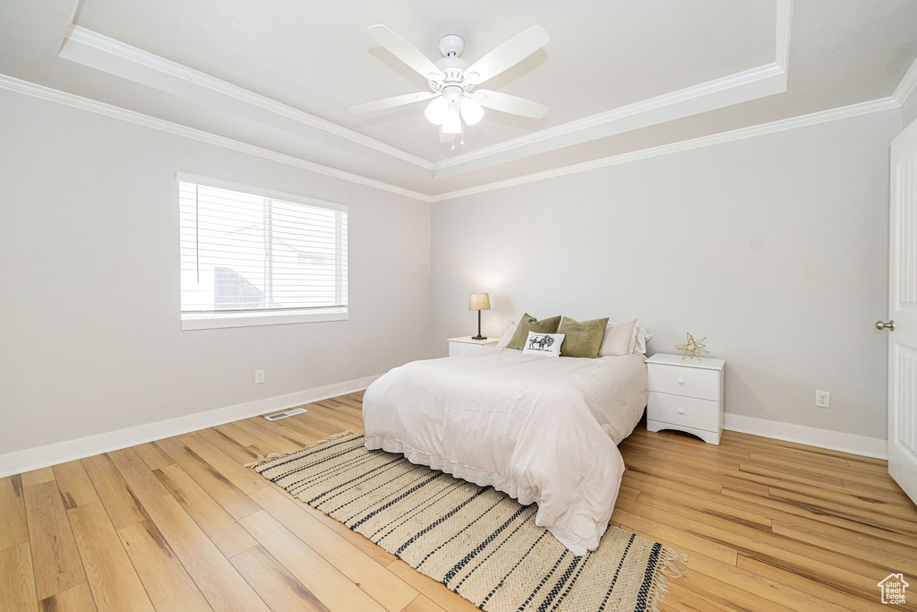 Bedroom featuring a tray ceiling, light wood-style flooring, crown molding, baseboards, and ceiling fan
