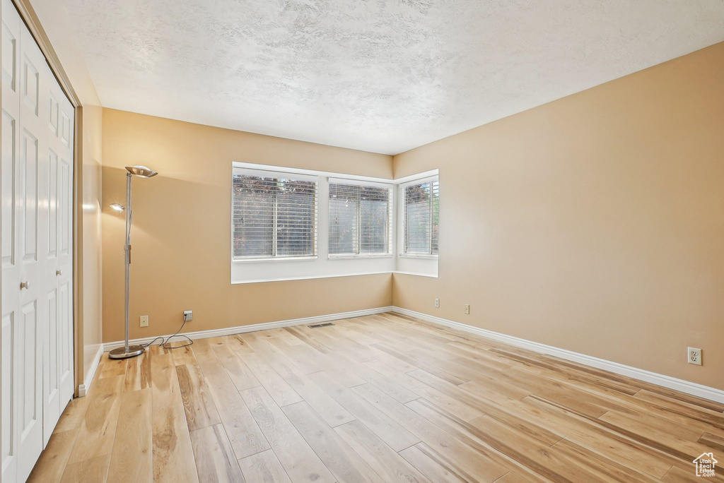 Spare room with light wood-style flooring, baseboards, and a textured ceiling