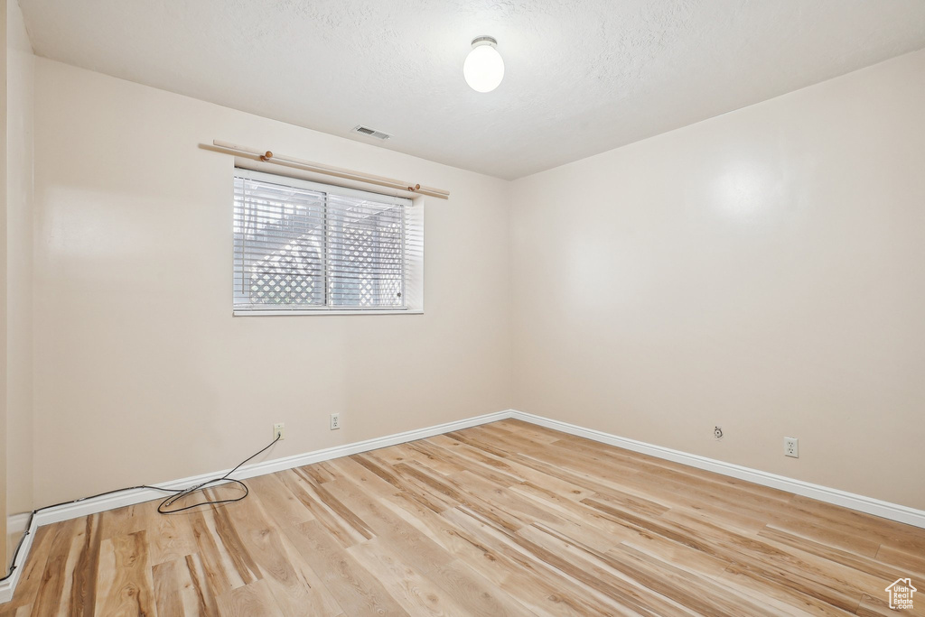 Unfurnished room featuring light wood finished floors, baseboards, and a textured ceiling