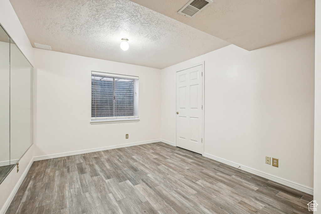 Spare room with wood finished floors, a textured ceiling, and baseboards