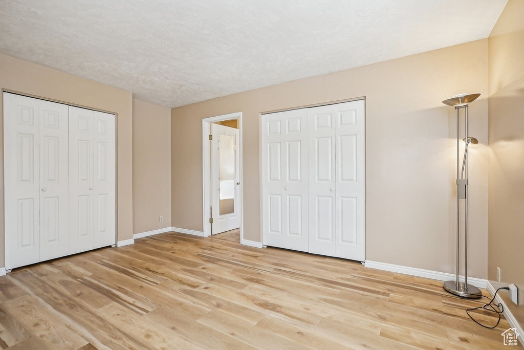Unfurnished bedroom featuring baseboards, light wood-style floors, and multiple closets