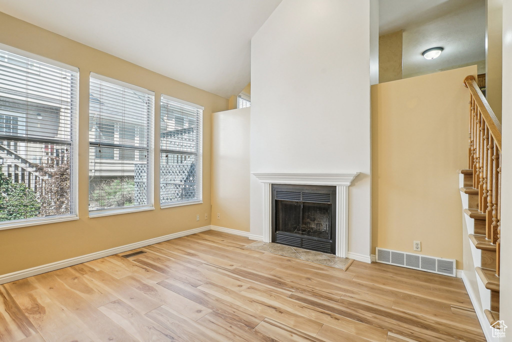 Unfurnished living room with a fireplace with flush hearth, stairs, wood finished floors, baseboards, and lofted ceiling