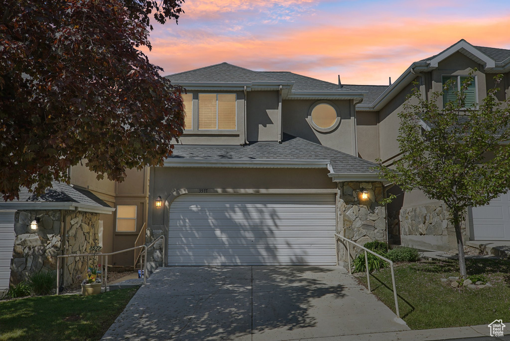 Traditional-style house featuring stucco siding, concrete driveway, stone siding, and a shingled roof