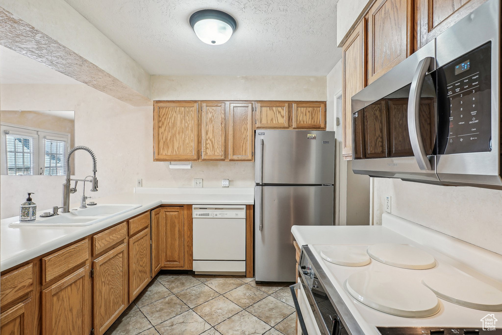 Kitchen featuring stainless steel appliances, a sink, light countertops, a textured ceiling, and light tile patterned floors