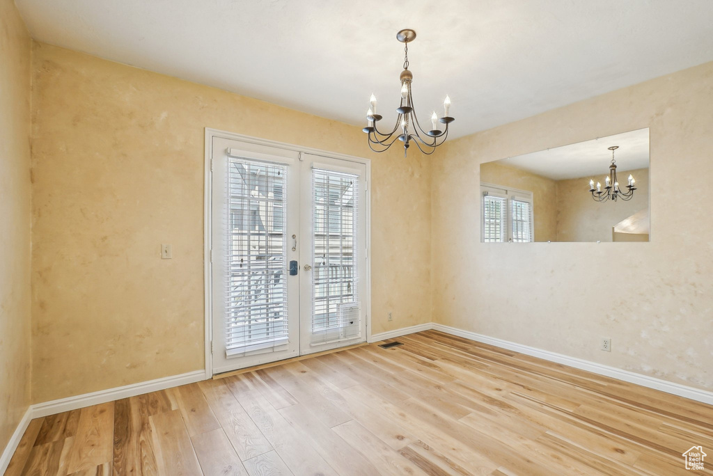 Spare room featuring a chandelier, wood-type flooring, baseboards, and french doors