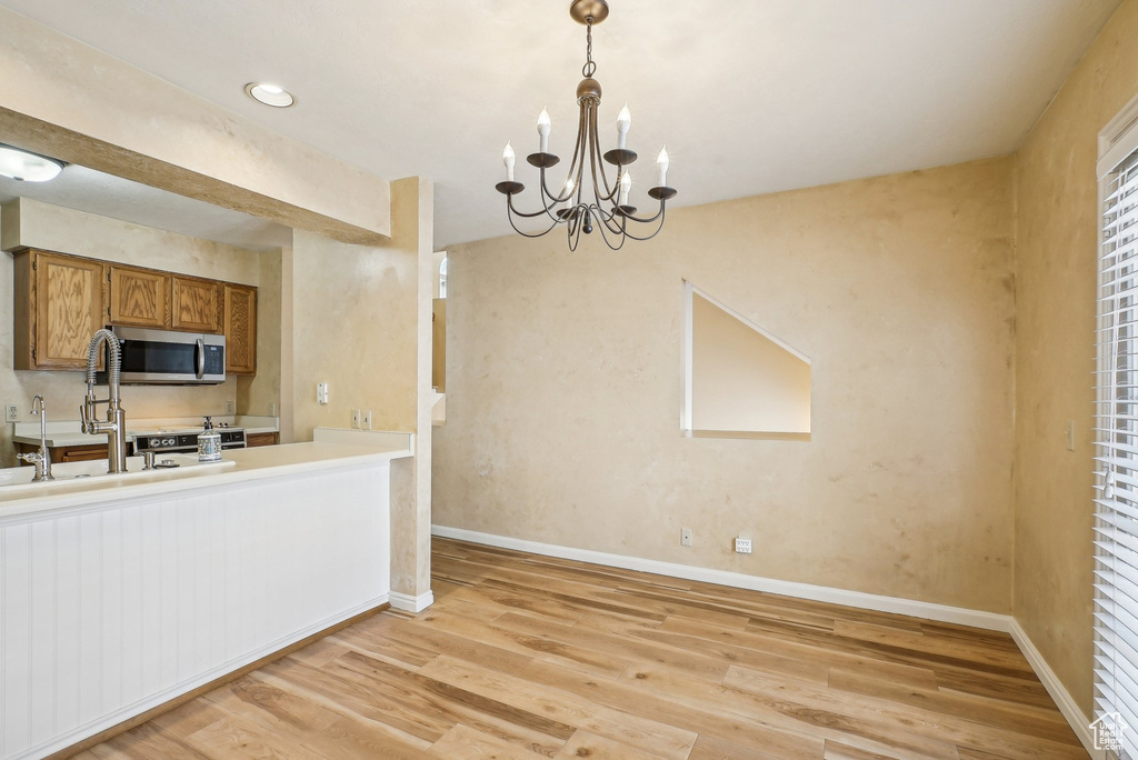 Kitchen featuring stainless steel microwave, brown cabinetry, light wood finished floors, a chandelier, and pendant lighting