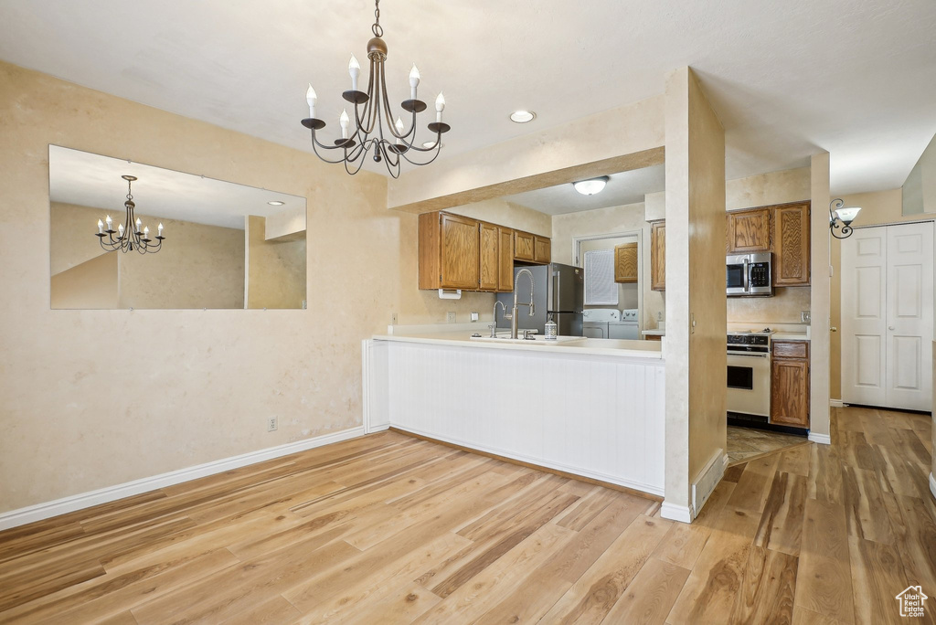 Kitchen with stainless steel appliances, a chandelier, a sink, brown cabinets, and light wood-type flooring