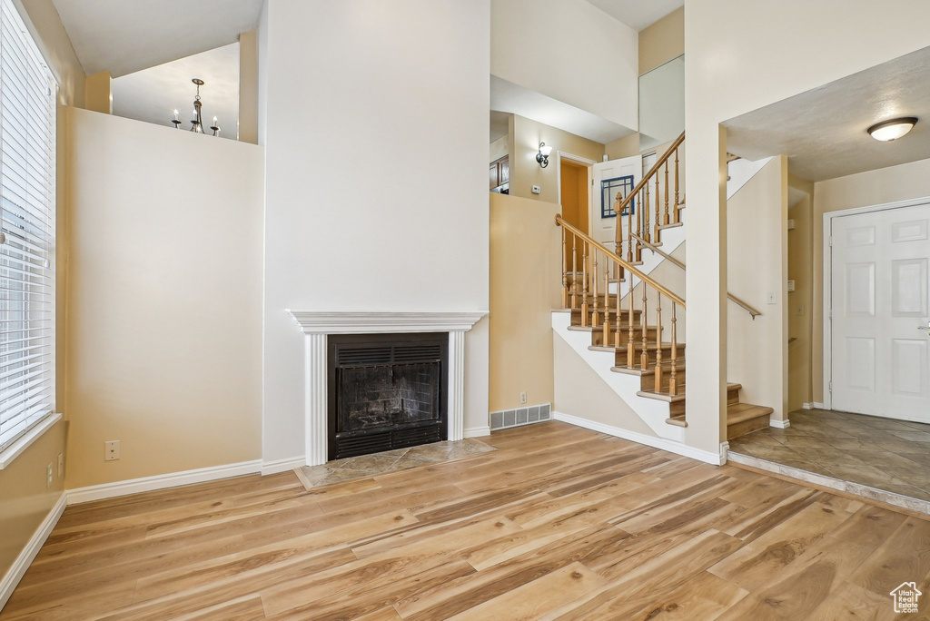 Unfurnished living room featuring a high ceiling, wood finished floors, stairs, a fireplace with flush hearth, and baseboards