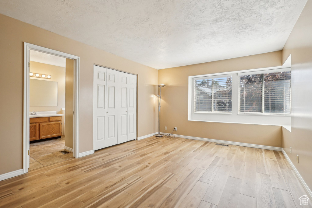 Unfurnished bedroom featuring light wood finished floors, a textured ceiling, baseboards, a closet, and ensuite bathroom