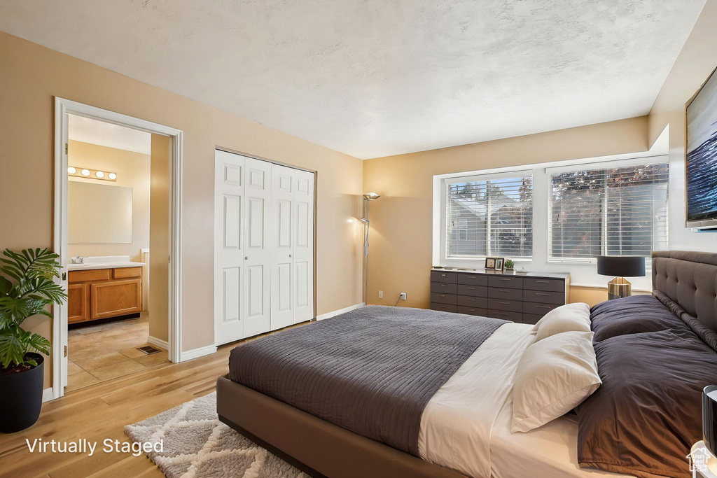 Bedroom featuring light wood finished floors, ensuite bath, a closet, and baseboards