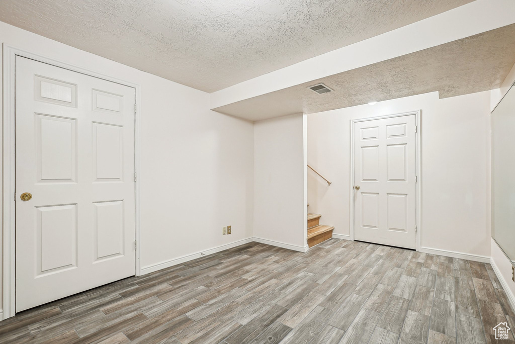 Below grade area with a textured ceiling, wood finished floors, stairs, and baseboards