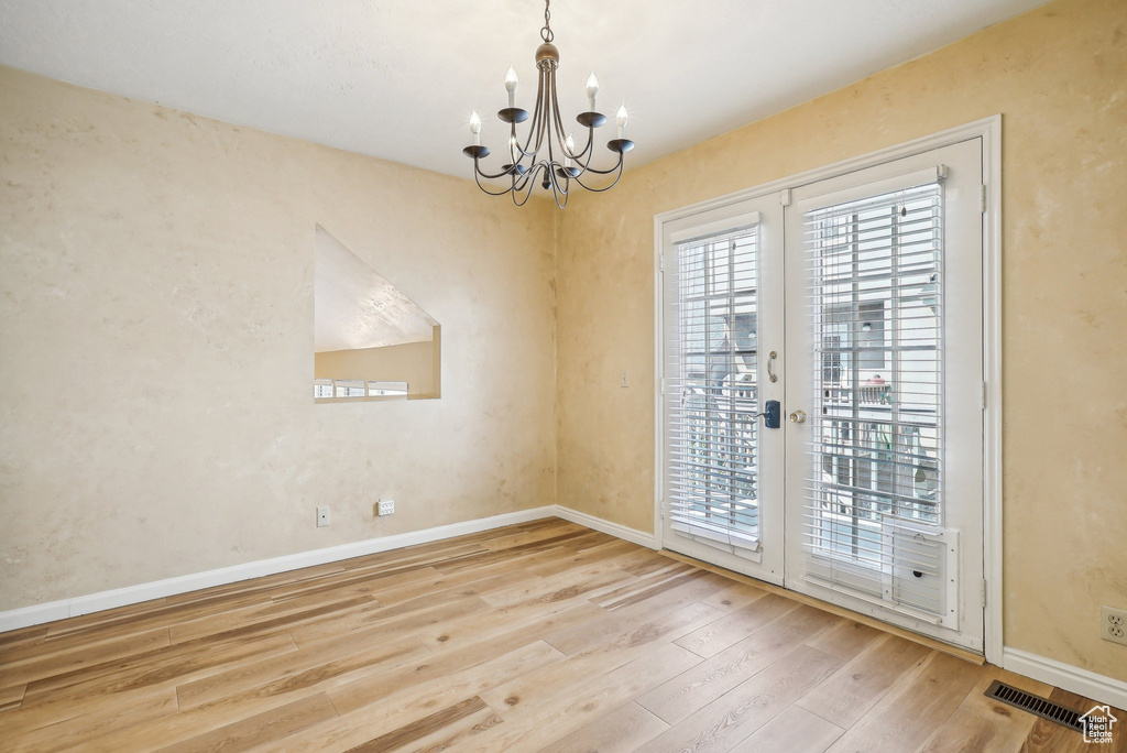 Unfurnished dining area with a chandelier, wood finished floors, and baseboards