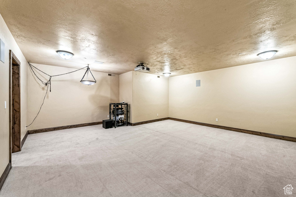 Finished basement featuring a textured ceiling, carpet, and baseboards
