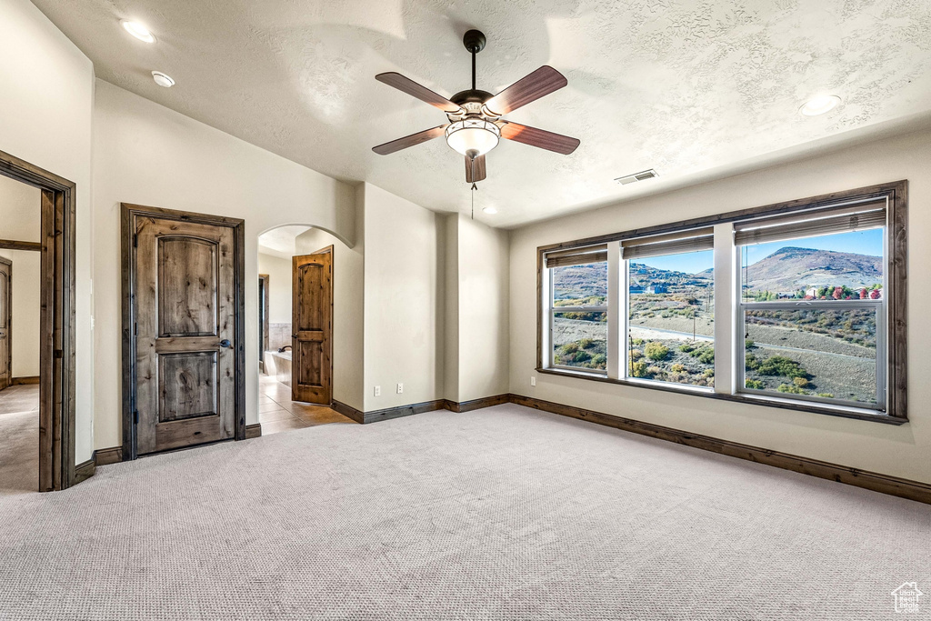 Unfurnished bedroom with arched walkways, light colored carpet, baseboards, a textured ceiling, and recessed lighting