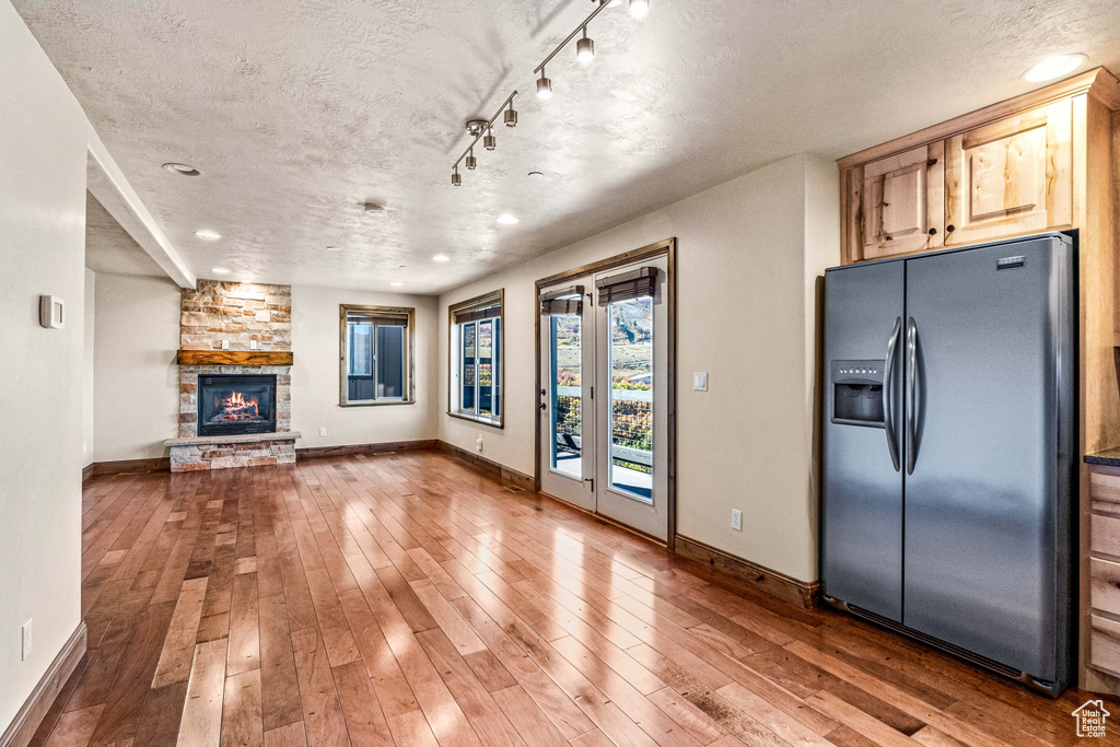 Unfurnished living room featuring baseboards, a textured ceiling, hardwood / wood-style flooring, a stone fireplace, and recessed lighting