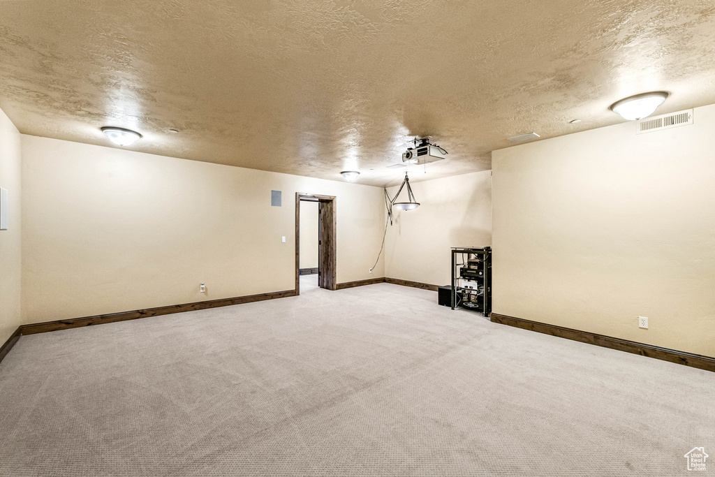 Finished below grade area with a textured ceiling, light carpet, and baseboards