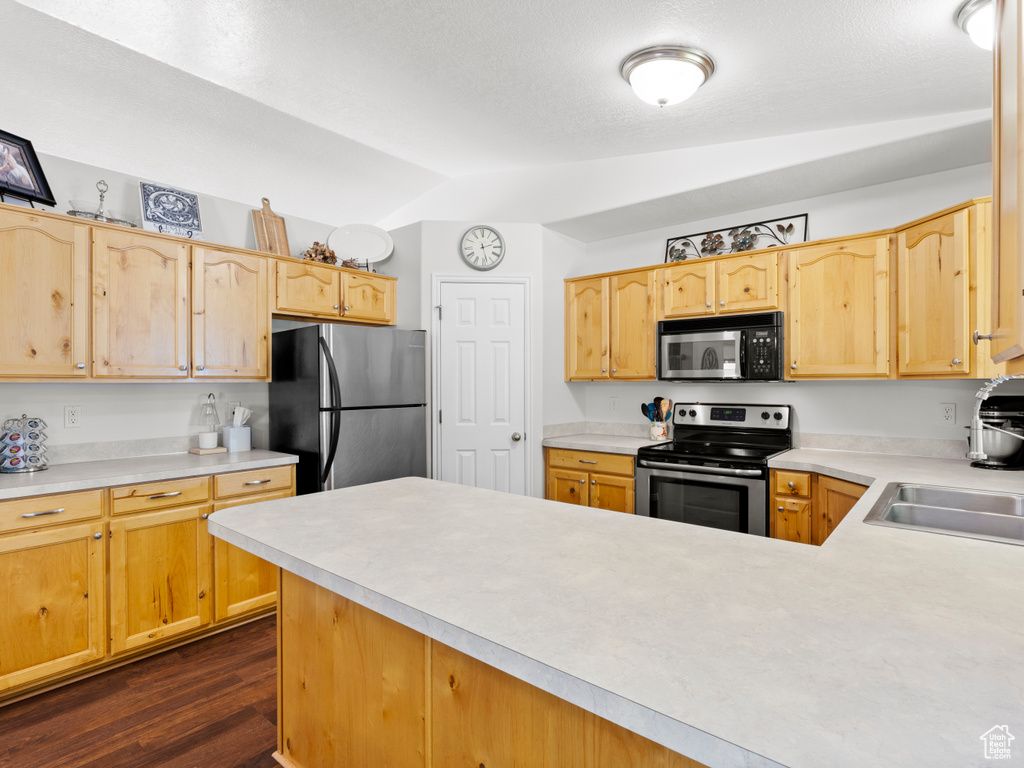 Kitchen featuring stainless steel appliances, vaulted ceiling, light countertops, dark wood-type flooring, and a peninsula