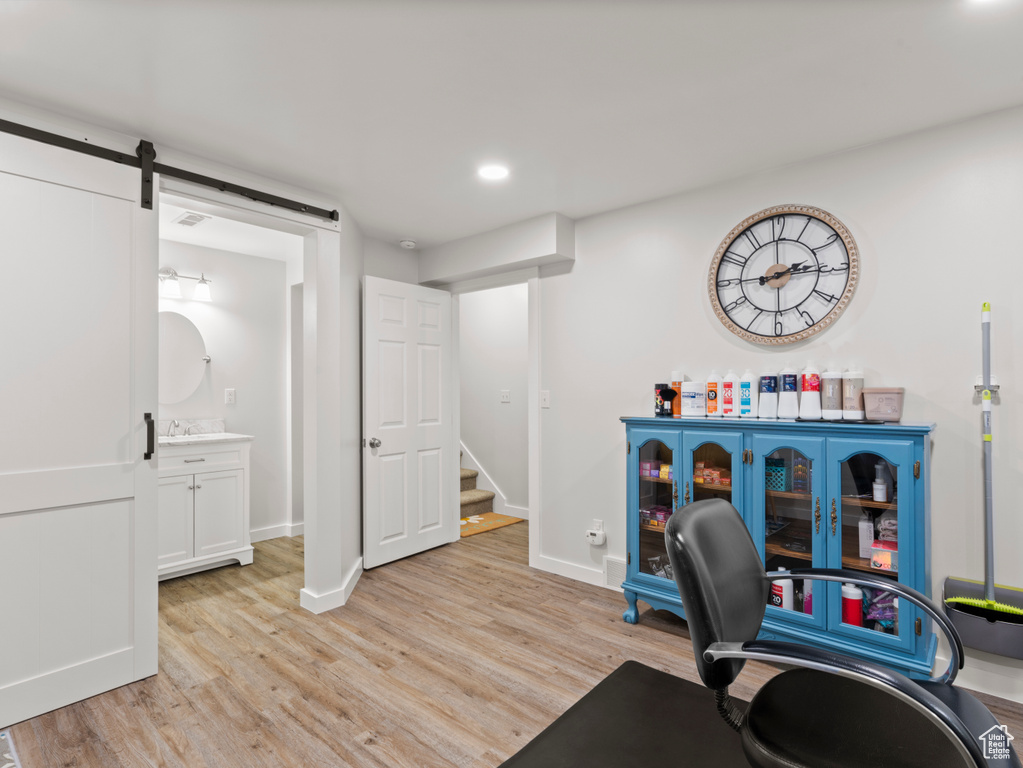 Office space featuring light wood finished floors, a barn door, baseboards, recessed lighting, and a sink