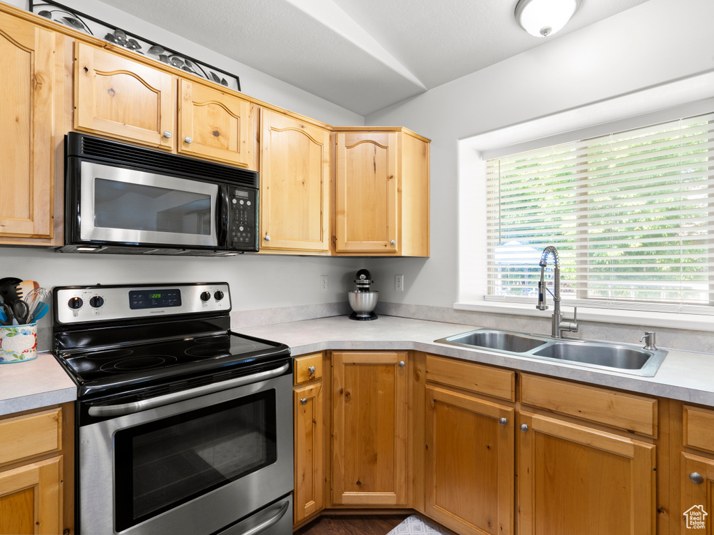 Kitchen with stainless steel range with electric stovetop, a sink, light countertops, and light brown cabinetry