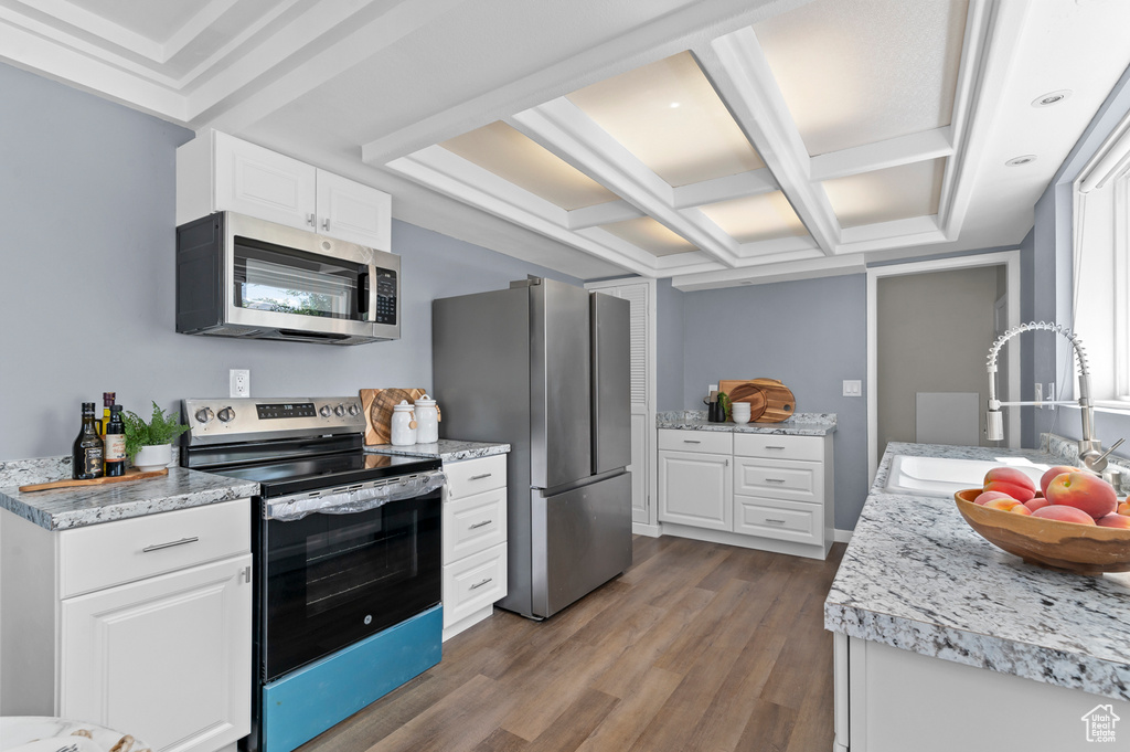 Kitchen featuring appliances with stainless steel finishes, a sink, coffered ceiling, wood finished floors, and white cabinetry