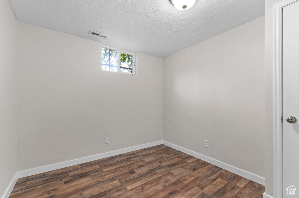 Empty room featuring dark wood finished floors, a textured ceiling, and baseboards