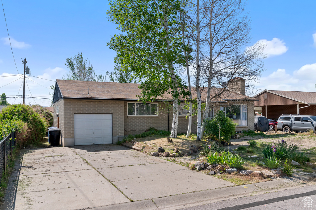 Ranch-style home with a garage, brick siding, driveway, fence, and a chimney