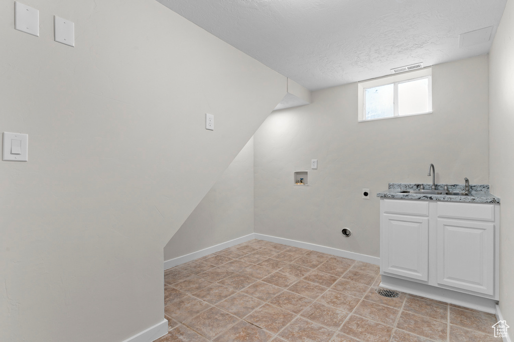 Laundry room with electric dryer hookup, hookup for a washing machine, a textured ceiling, baseboards, and cabinet space