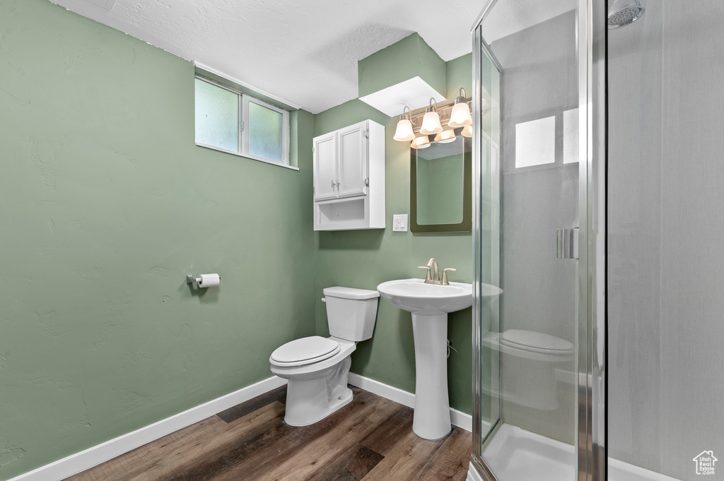 Bathroom featuring toilet, a stall shower, wood finished floors, baseboards, and a chandelier