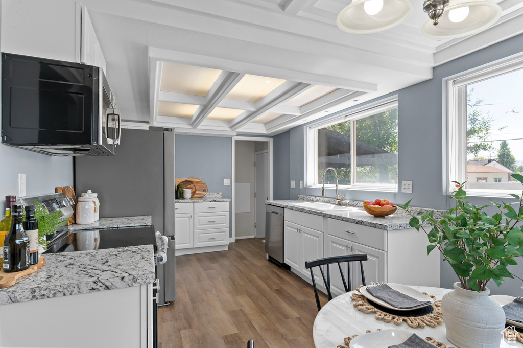 Kitchen featuring appliances with stainless steel finishes, a sink, white cabinets, wood finished floors, and beamed ceiling