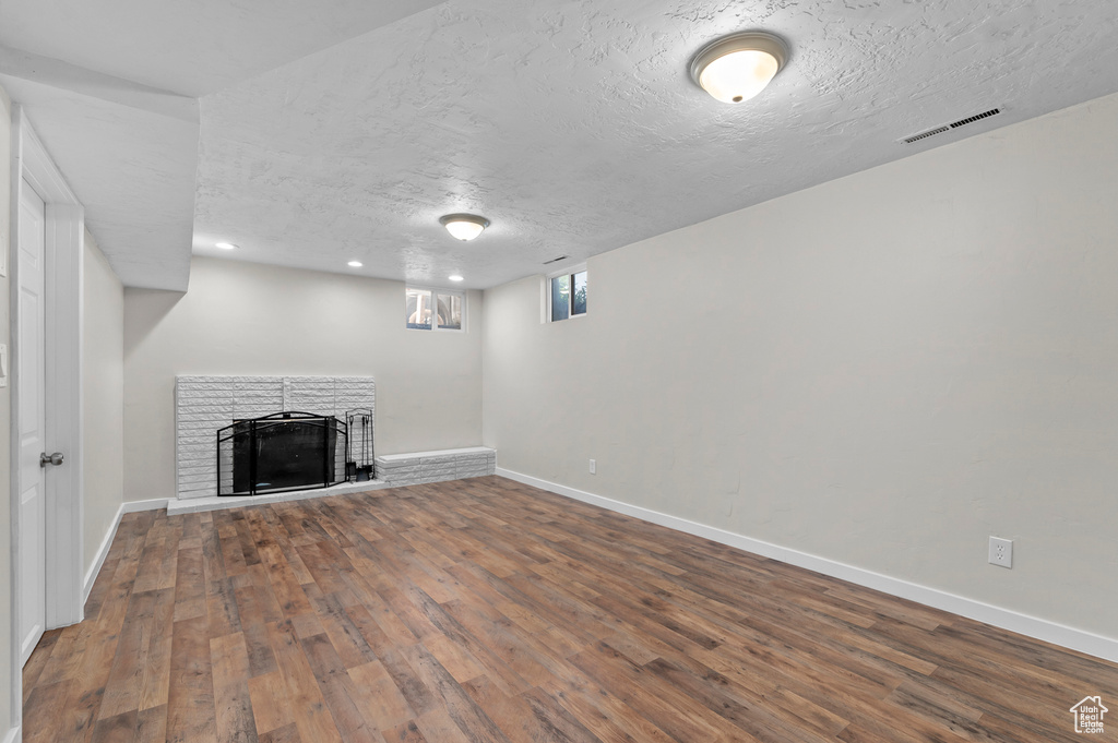 Below grade area with wood finished floors, a textured ceiling, baseboards, and a stone fireplace