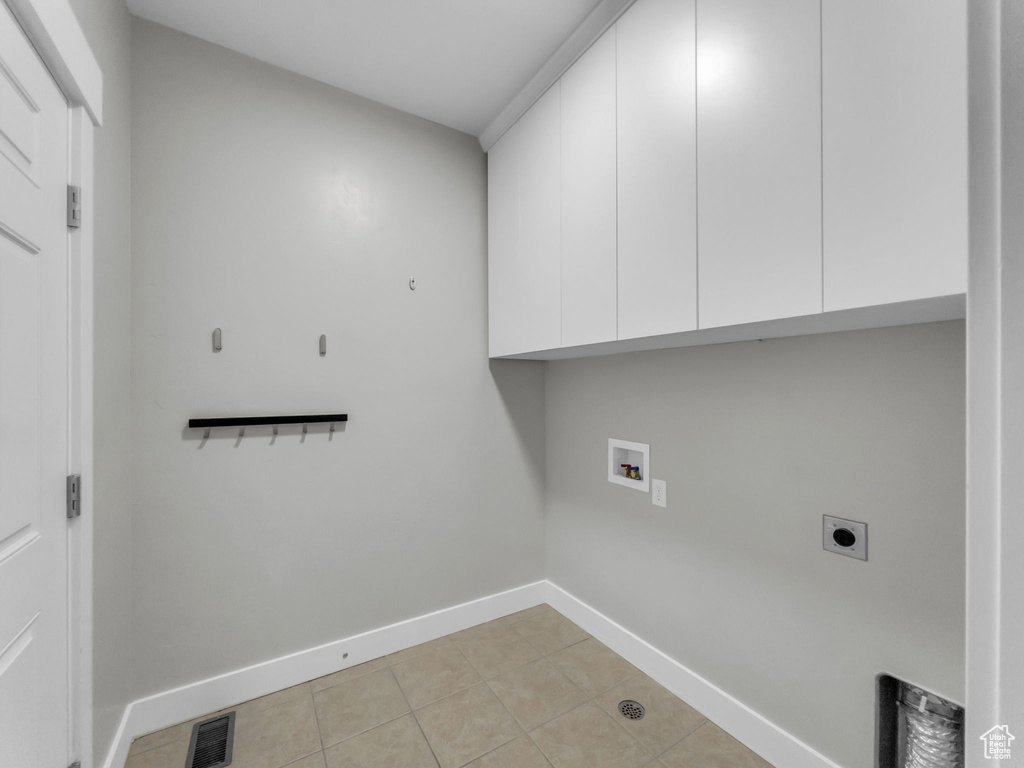 Laundry room featuring cabinet space, electric dryer hookup, light tile patterned floors, baseboards, and hookup for a washing machine