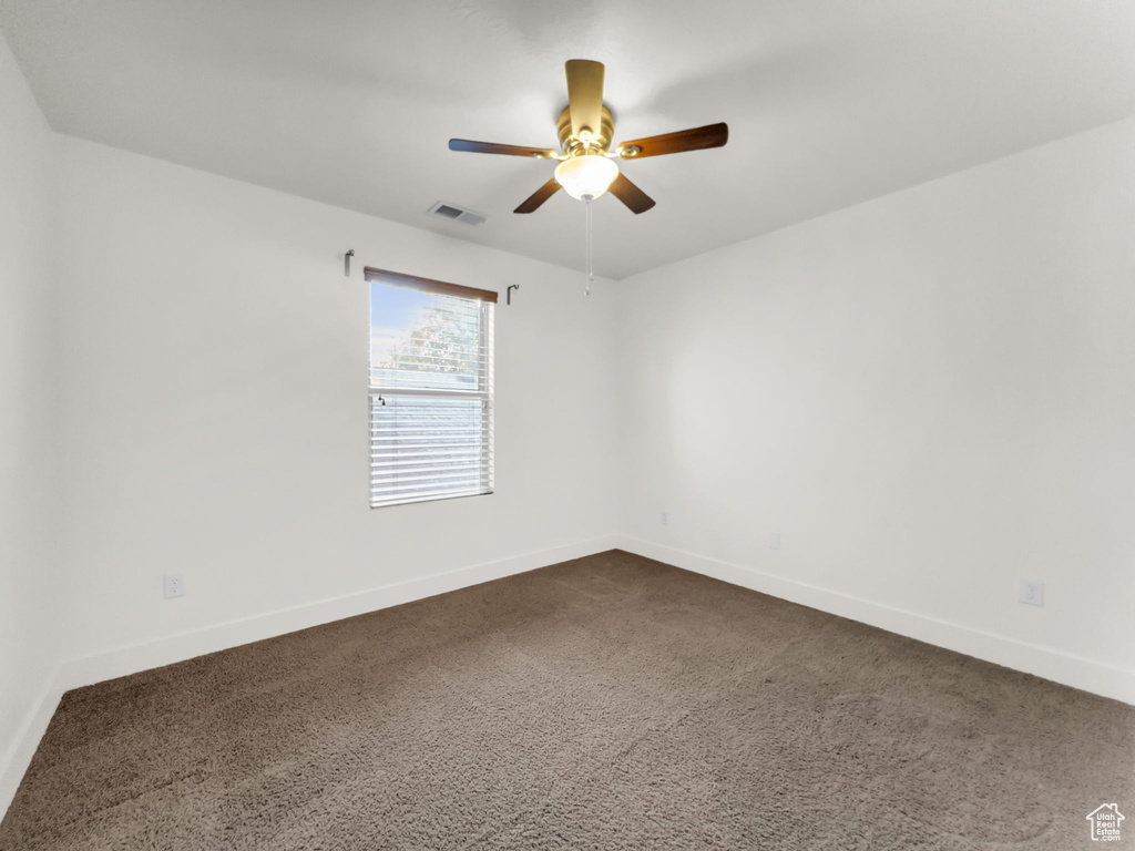 Spare room featuring a ceiling fan, dark colored carpet, and baseboards