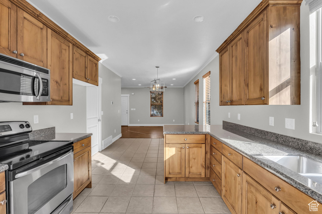 Kitchen with stainless steel appliances, light tile patterned floors, a peninsula, brown cabinetry, and recessed lighting