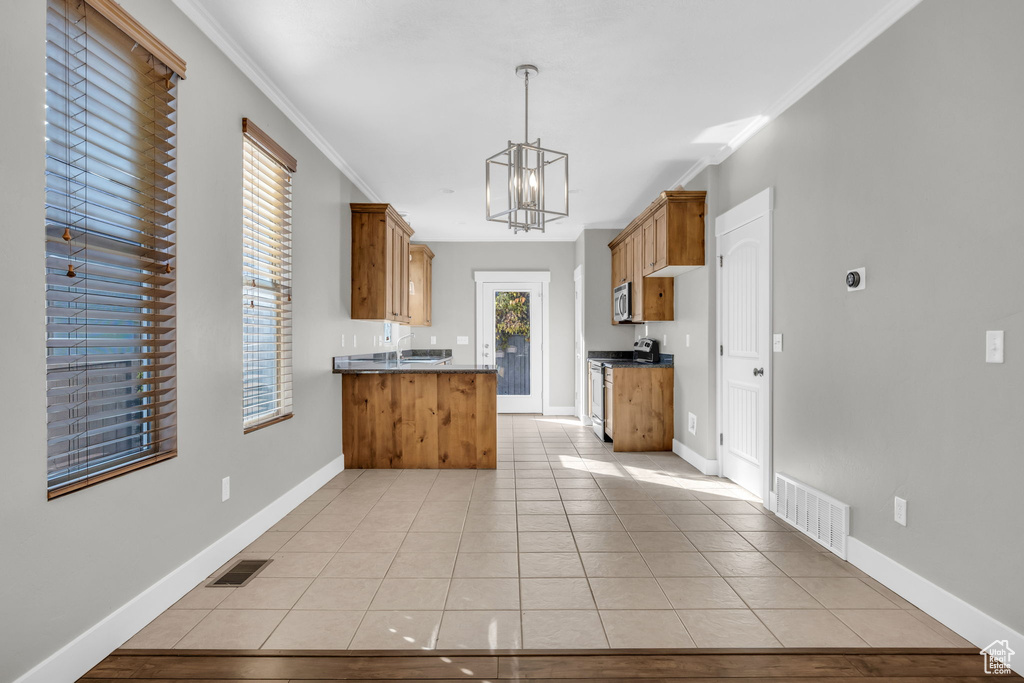 Kitchen featuring appliances with stainless steel finishes, dark countertops, a chandelier, crown molding, and brown cabinetry