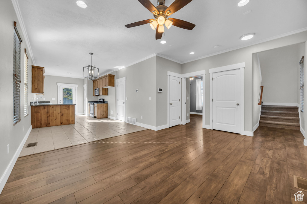 Unfurnished living room with a ceiling fan, baseboards, stairs, wood finished floors, and crown molding