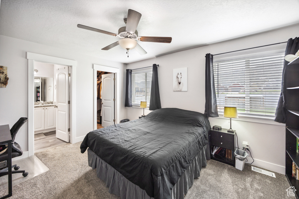 Bedroom featuring light colored carpet, connected bathroom, a ceiling fan, a spacious closet, and baseboards