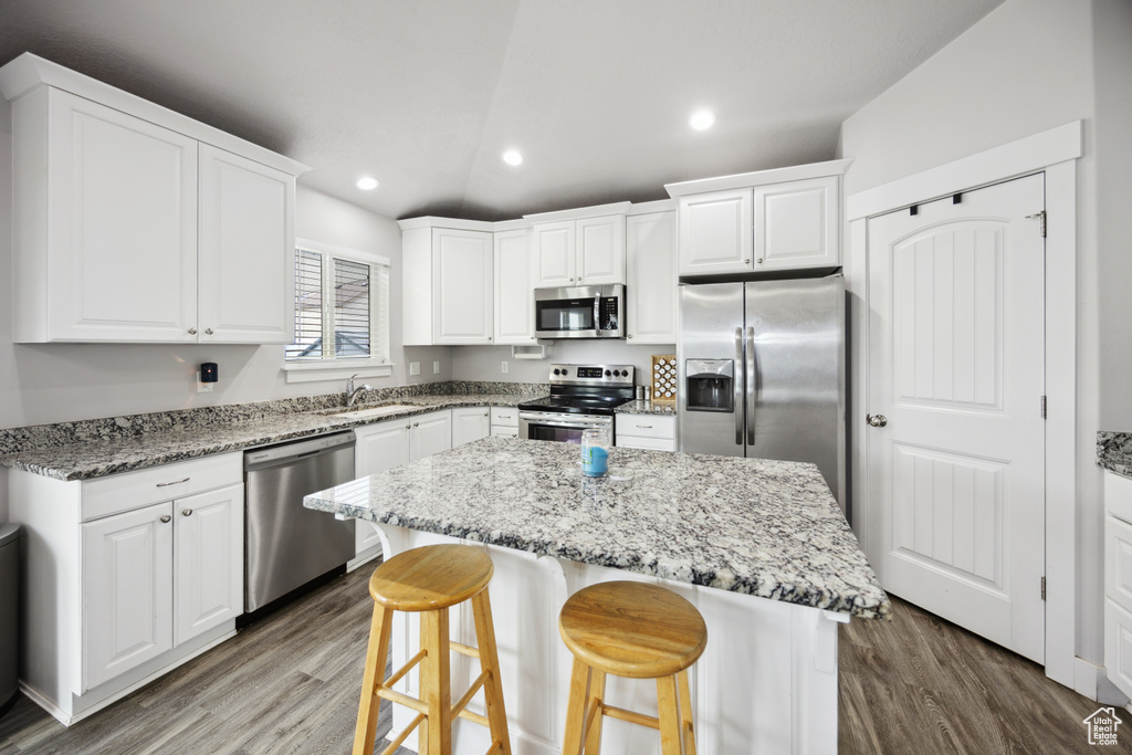 Kitchen featuring stainless steel appliances, a sink, wood finished floors, a kitchen bar, and white cabinetry
