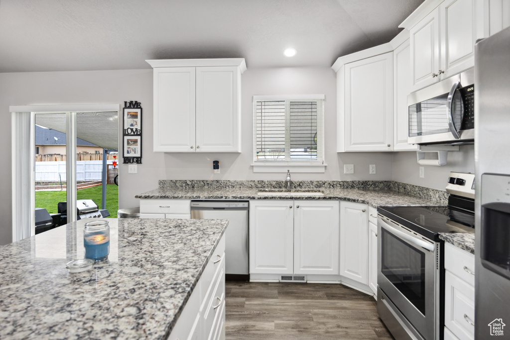 Kitchen with stainless steel appliances, a sink, wood finished floors, white cabinetry, and recessed lighting