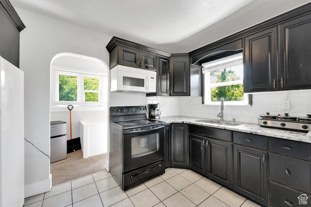Kitchen with white appliances, a sink, light carpet, light stone counters, and backsplash