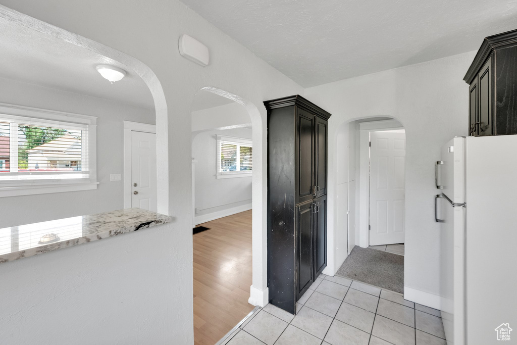 Kitchen with freestanding refrigerator, light stone counters, arched walkways, light tile patterned floors, and baseboards