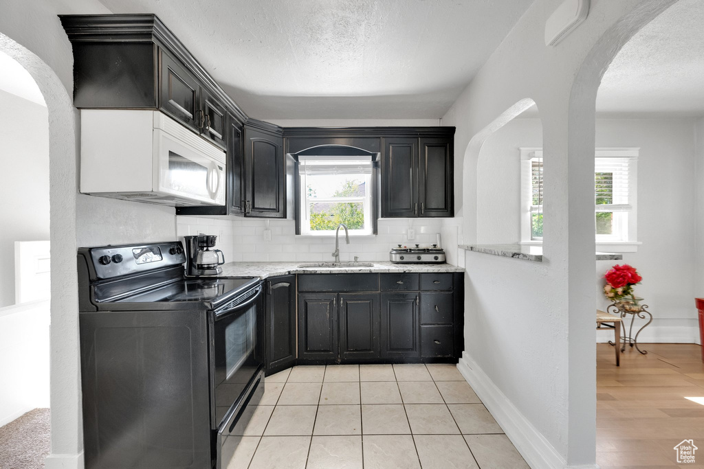 Kitchen with black range with electric cooktop, white microwave, a sink, arched walkways, and plenty of natural light