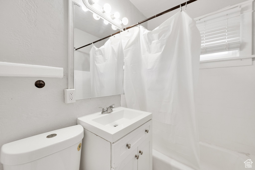 Full bath featuring toilet, vanity, a textured wall, and shower / bathtub combination with curtain