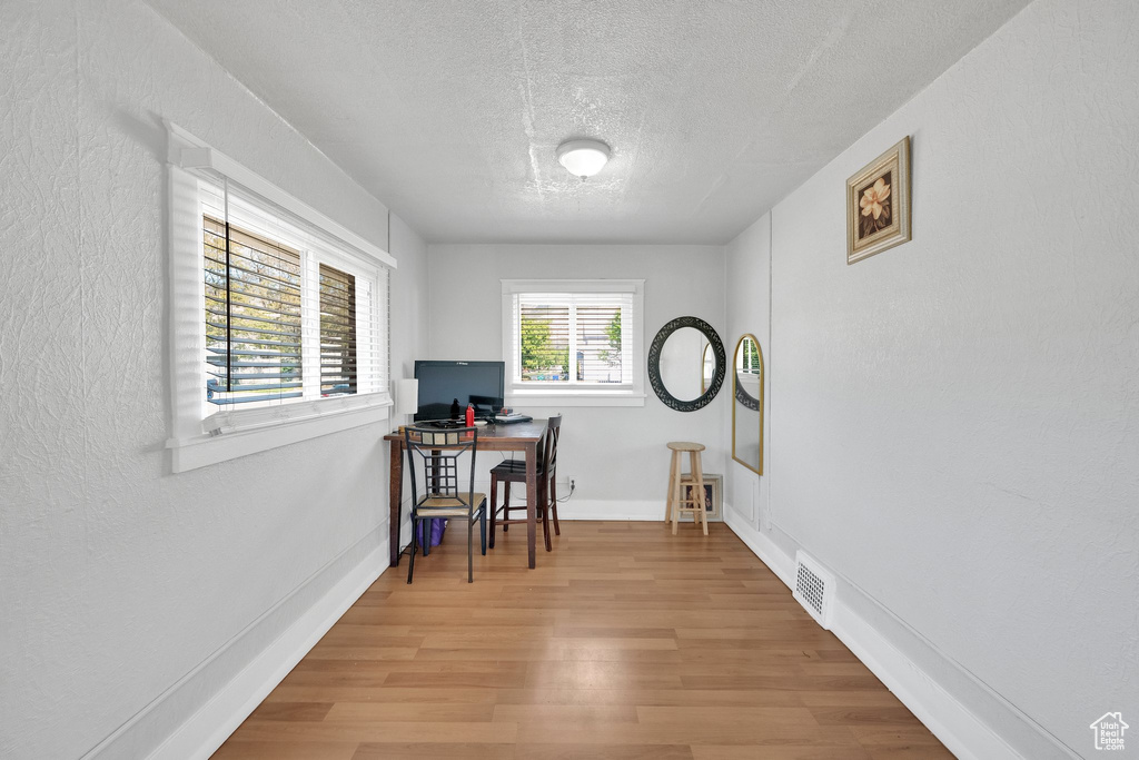 Office area with a textured ceiling, light wood-type flooring, baseboards, and a textured wall