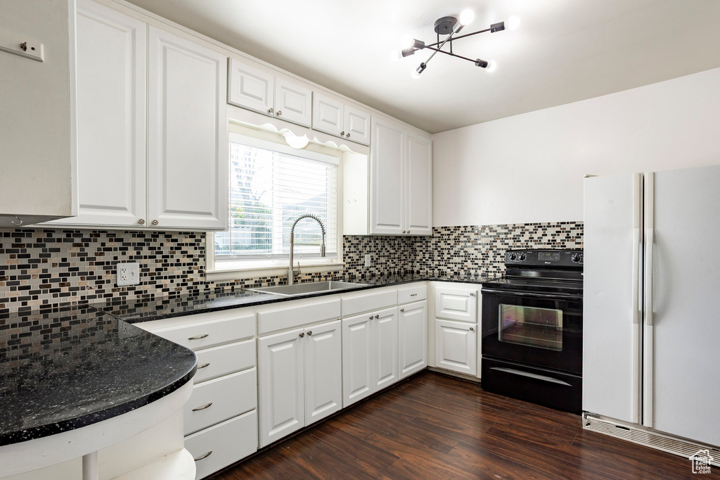 Kitchen with freestanding refrigerator, black electric range oven, a sink, and white cabinetry