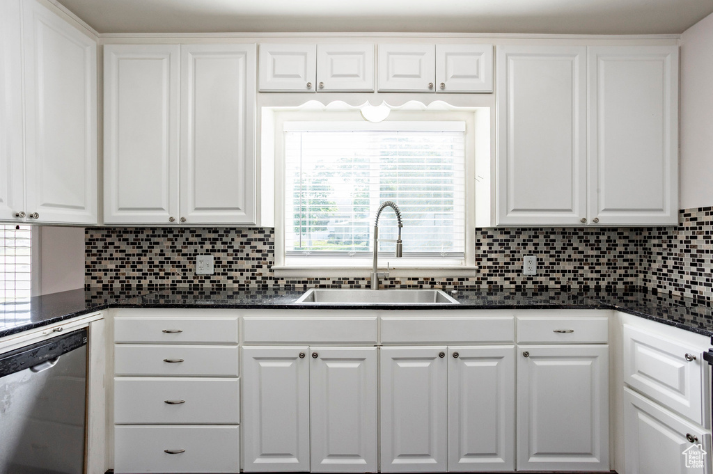 Kitchen with stainless steel dishwasher, a sink, and white cabinetry