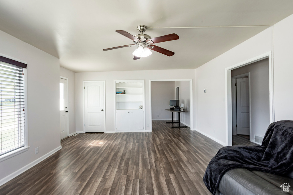 Living room featuring baseboards, built in features, a ceiling fan, and dark wood-type flooring