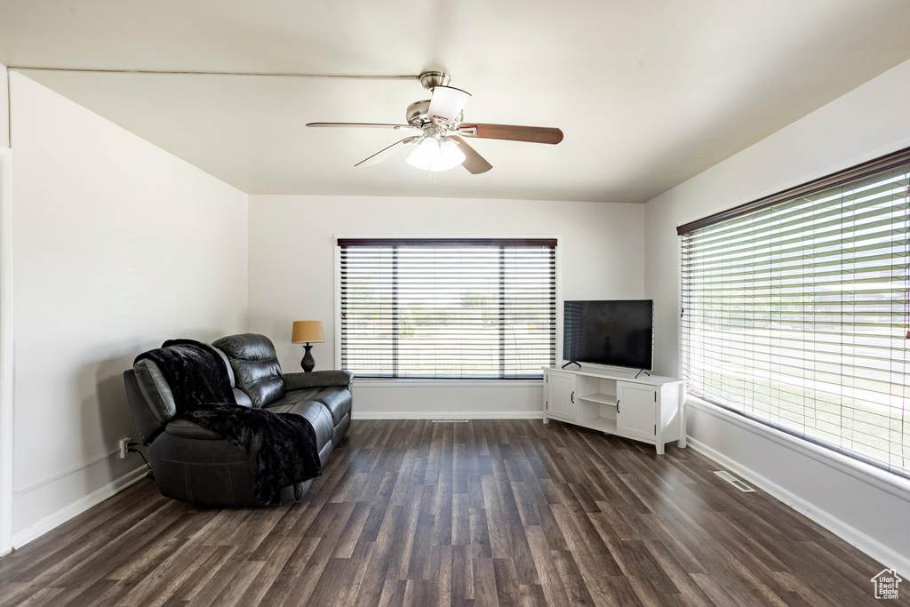 Living area featuring dark wood-style floors, a ceiling fan, and baseboards