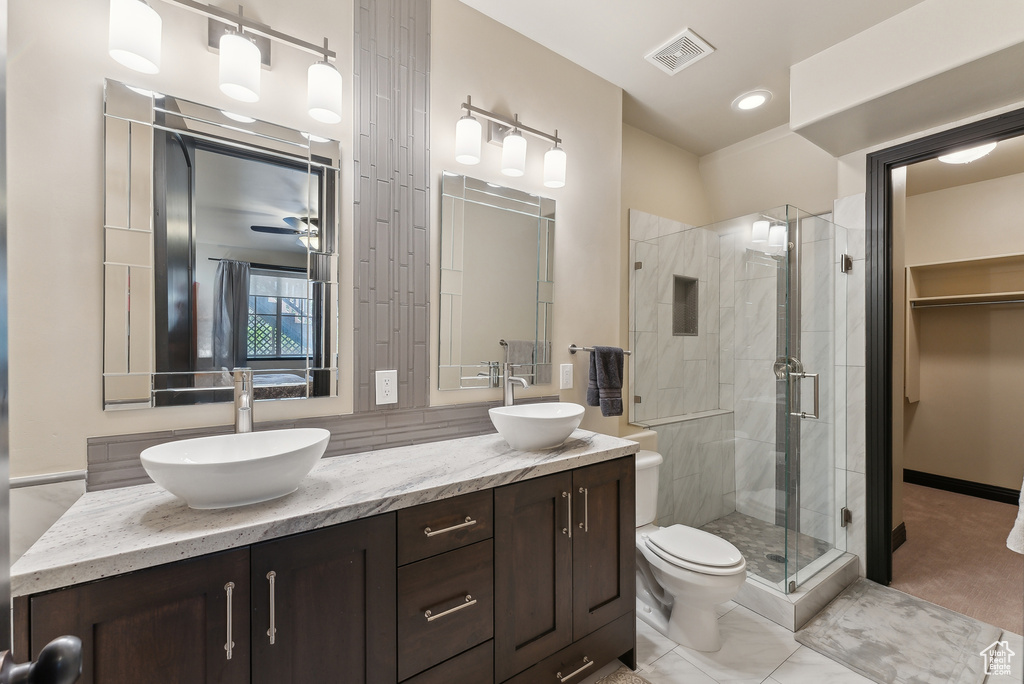 Full bathroom featuring a shower stall, double vanity, toilet, and ceiling fan
