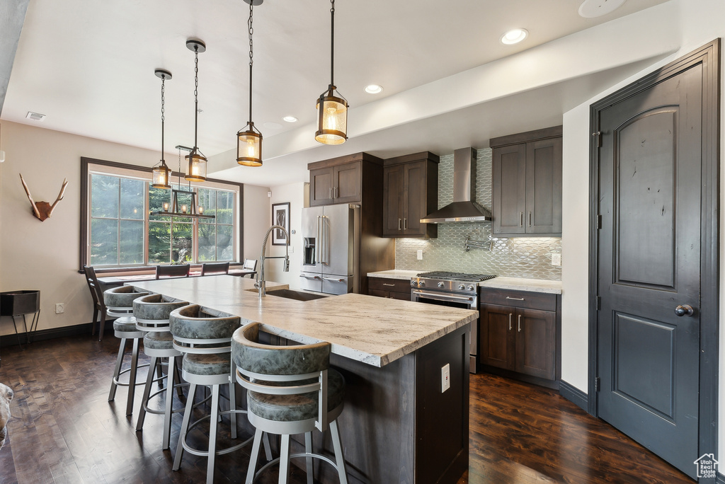 Kitchen with wall chimney exhaust hood, high end appliances, a sink, light countertops, and dark wood finished floors